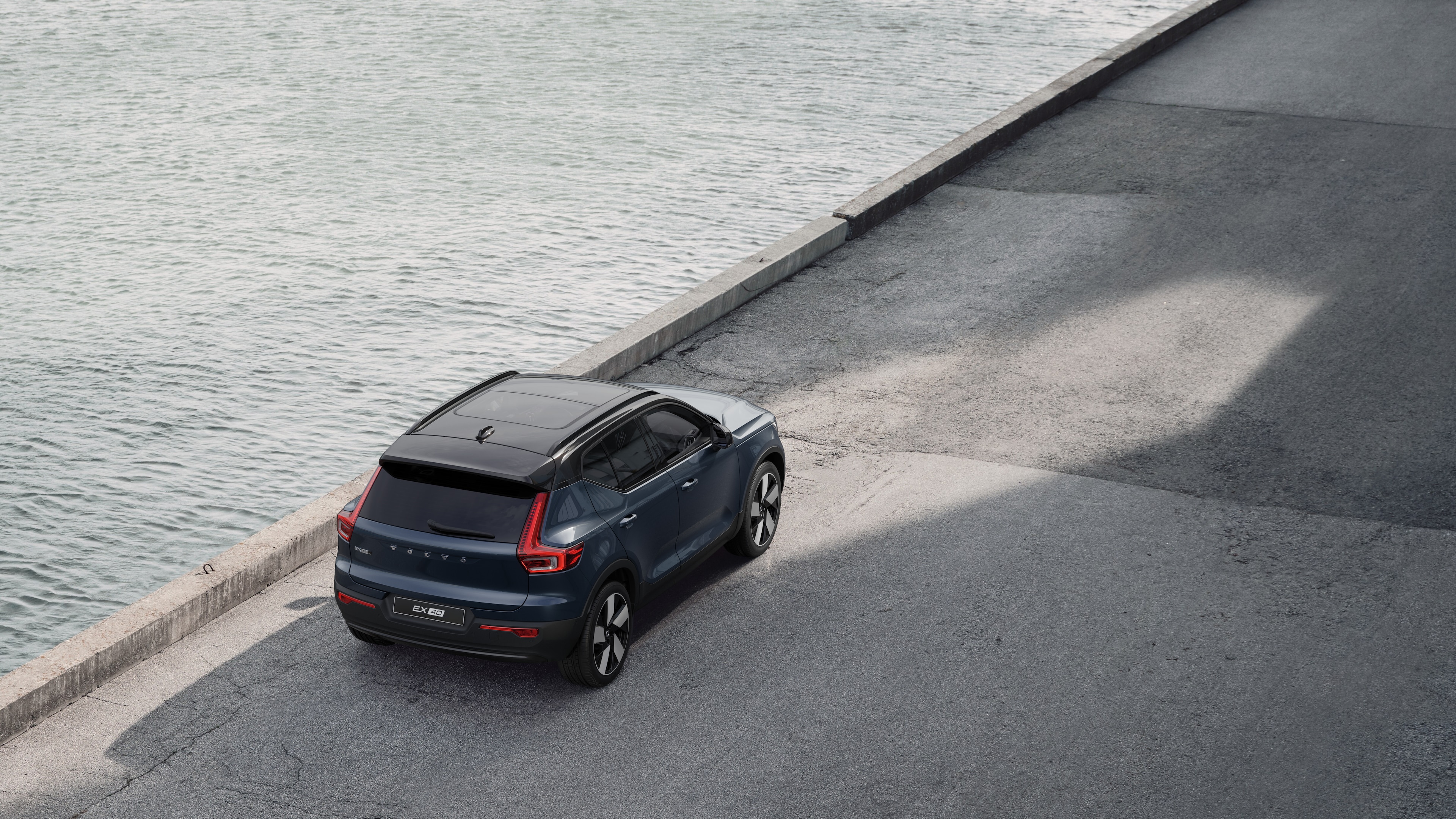 Vue arrière d’une voiture Volvo garée dans une rue calme au bord de l’eau, avec une allée pavée et de l’eau en arrière-plan.