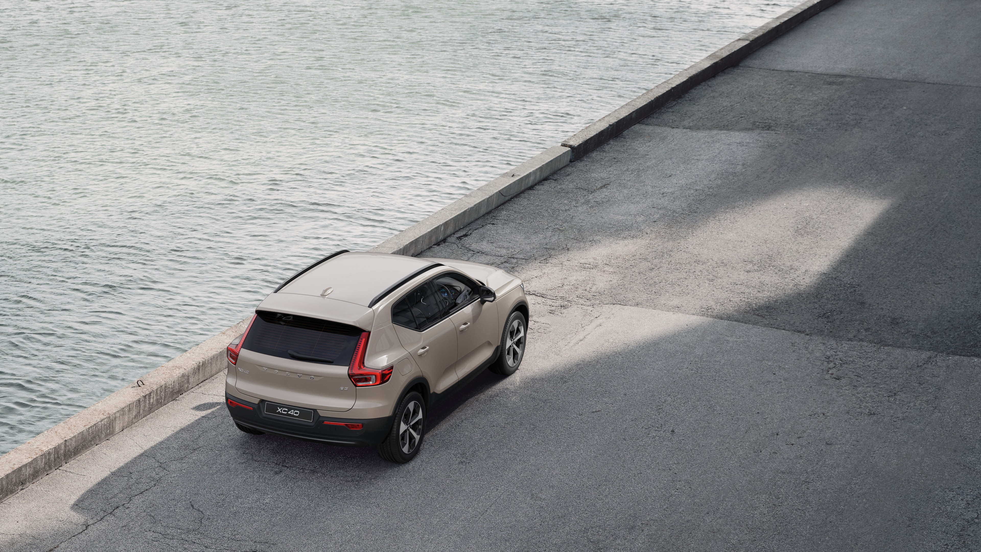 Volvo car rear view parked on quiet street beside water, with a paved walkway and water as the background.