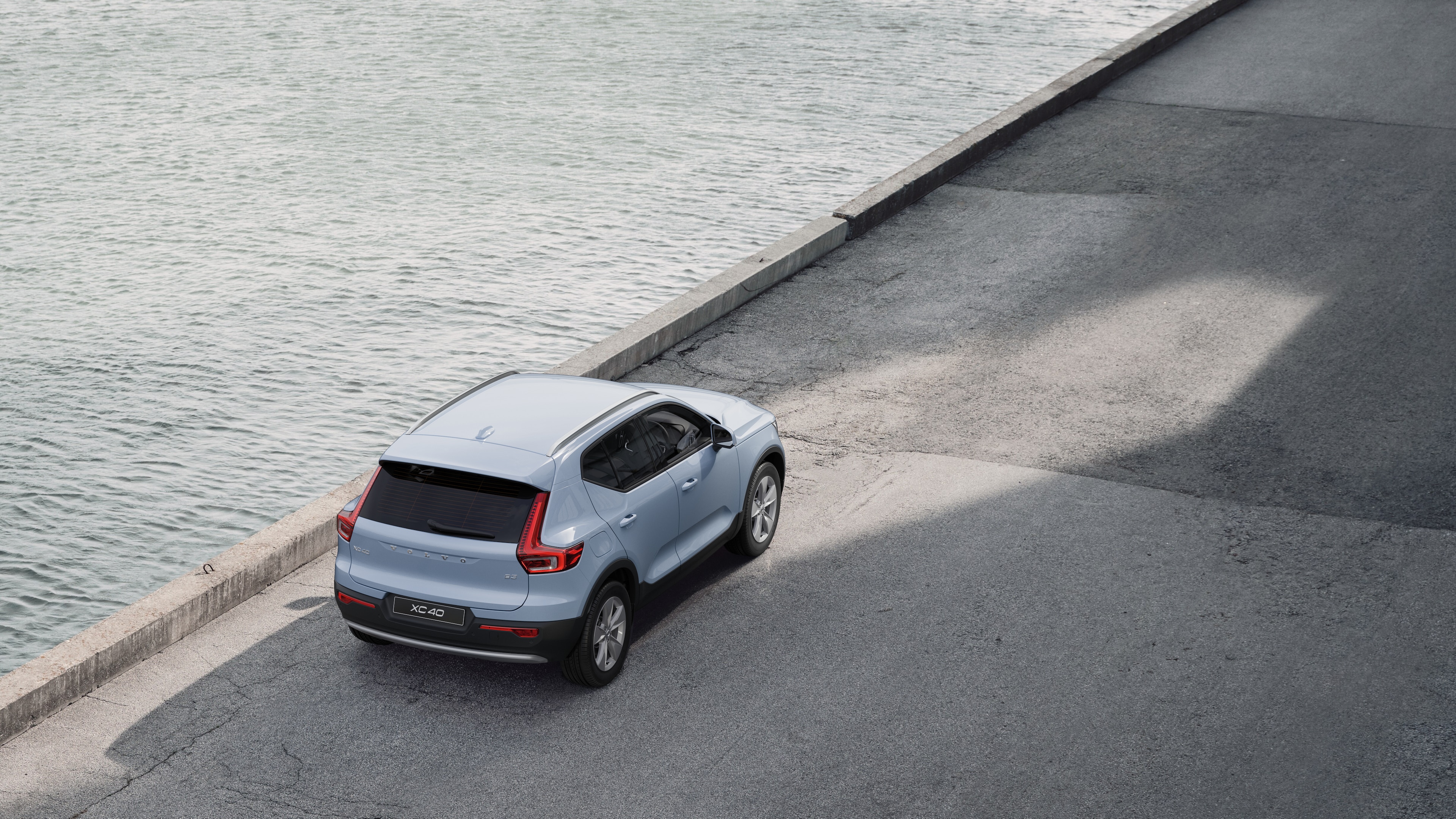 Volvo car rear view parked on quiet street beside water, with a paved walkway and water as the background.