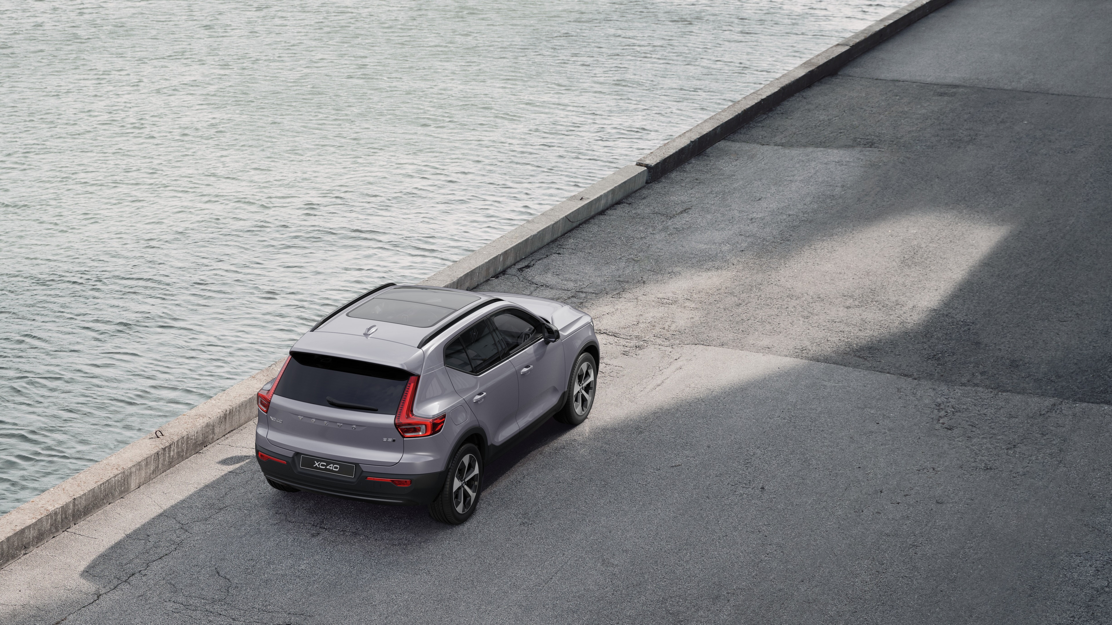 Volvo car rear view parked on quiet street beside water, with a paved walkway and water as the background.