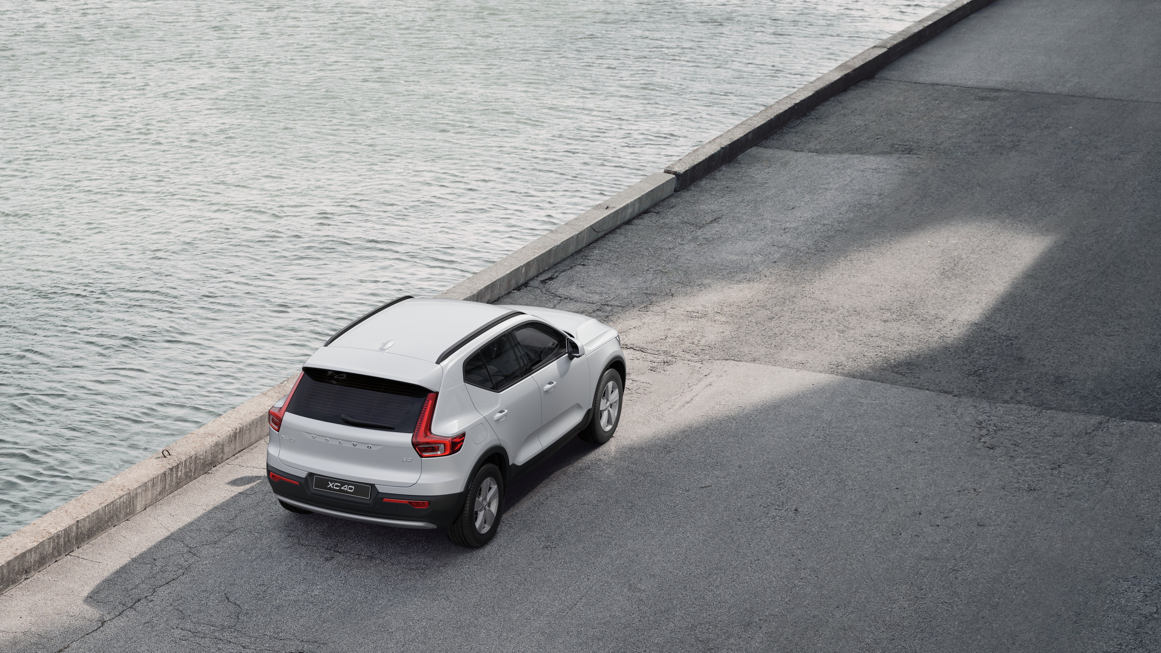 Vista posteriore di un'auto Volvo parcheggiata in una strada tranquilla accanto all'acqua, con un passaggio pedonale lastricato e l'acqua sullo sfondo.