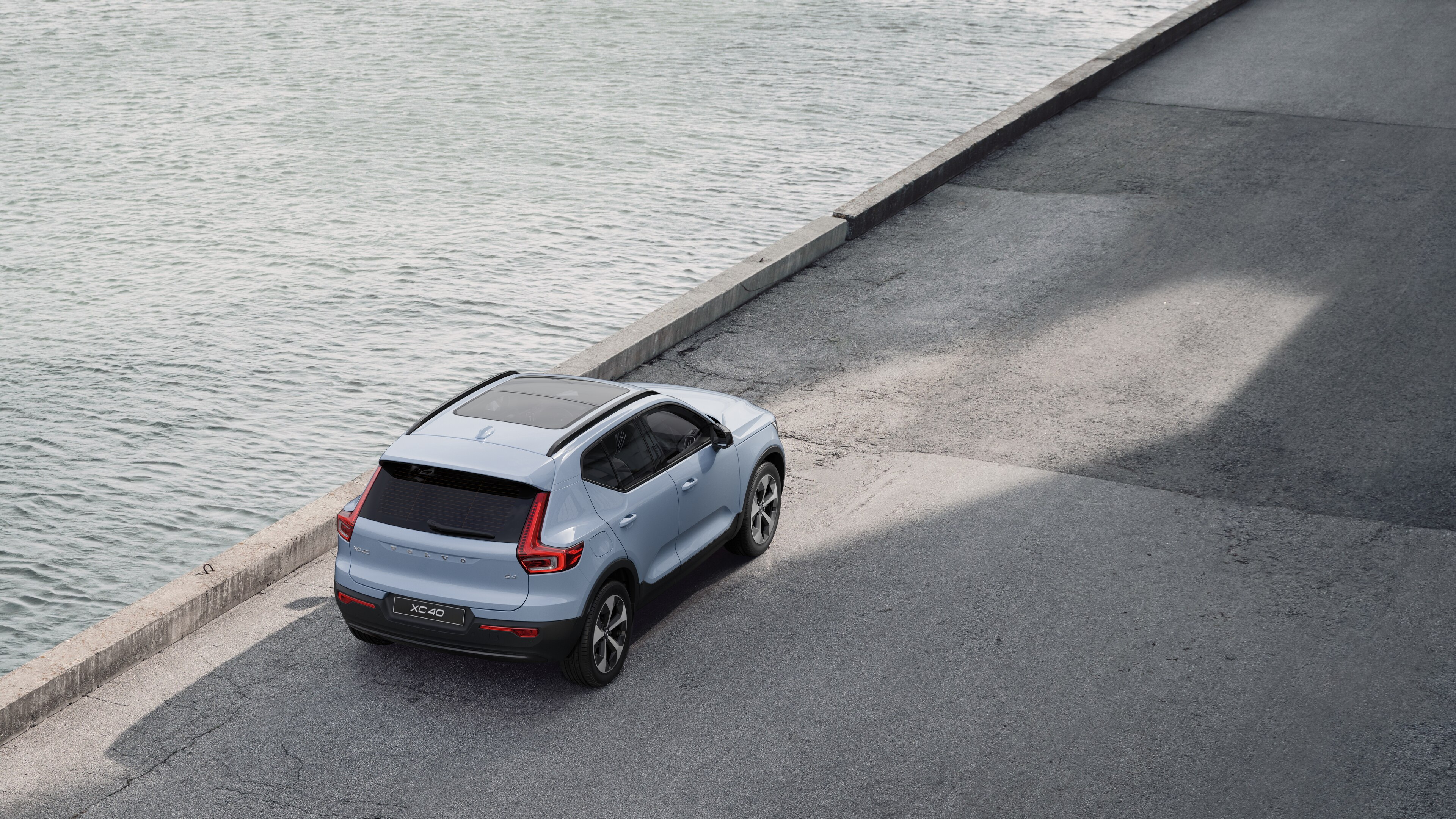 Автомобіль Volvo, вигляд ззаду, припаркований на тихій вулиці біля води, на тлі асфальтованої доріжки та води.