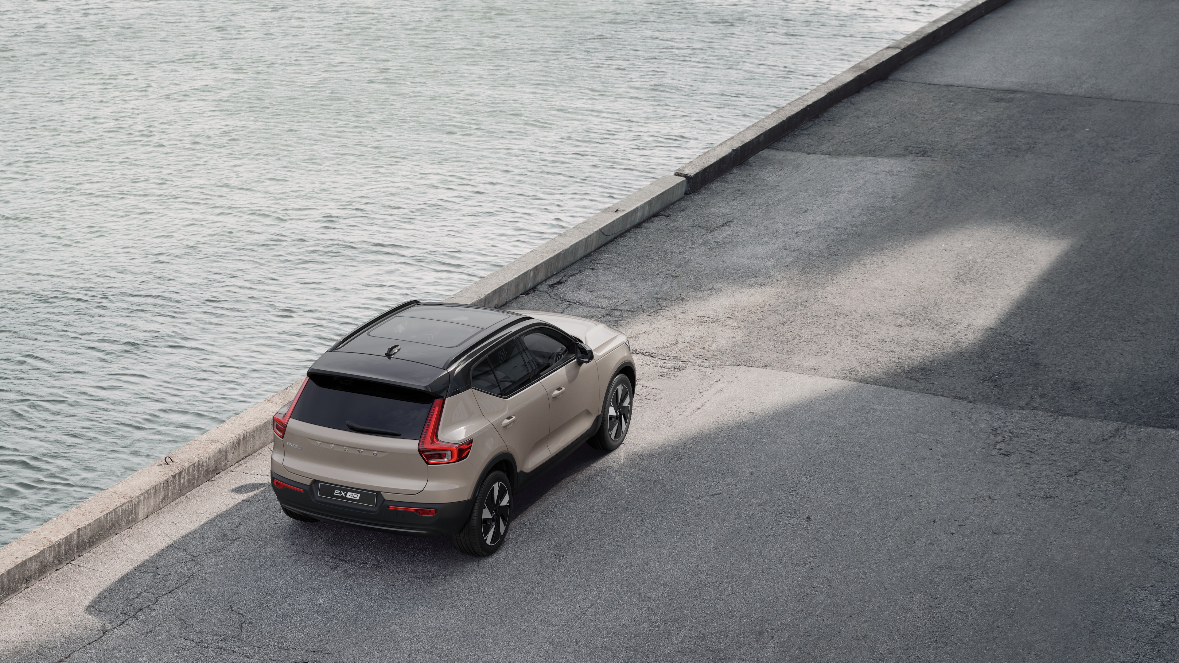 Achteraanzicht van een Volvo geparkeerd in een rustige straat aan het water, met een geplaveid looppad en water als achtergrond.
