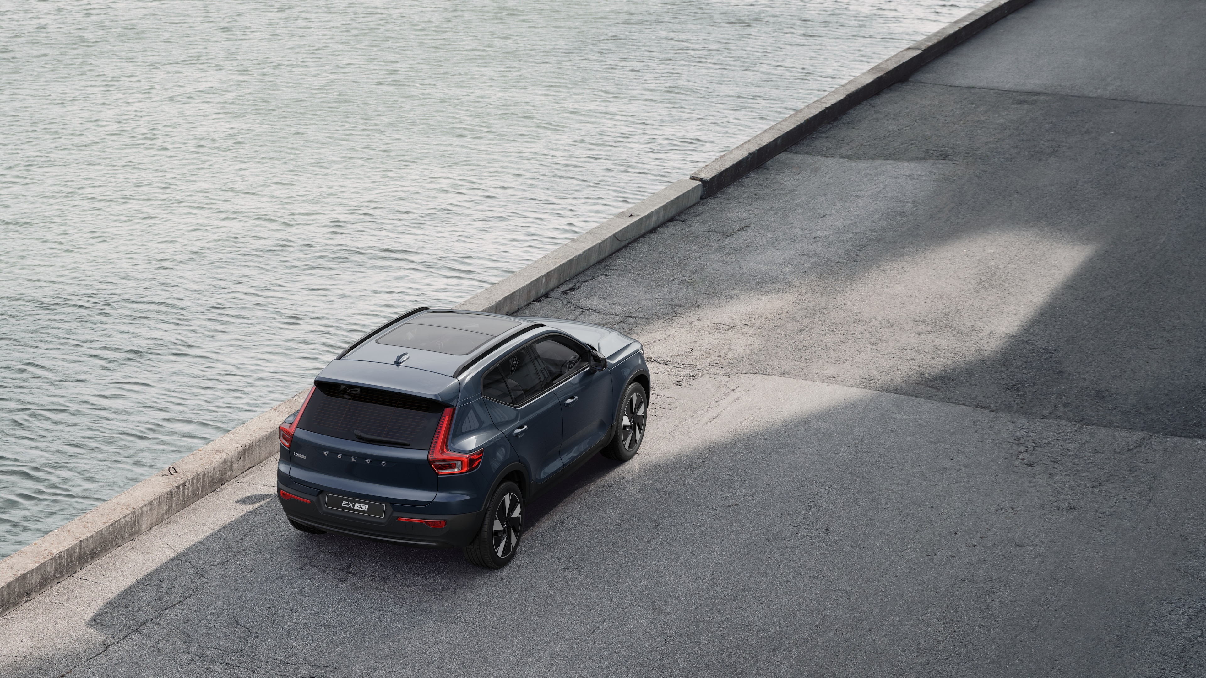 Volvo car rear view parked on quiet street beside water, with a paved walkway and water as the background.