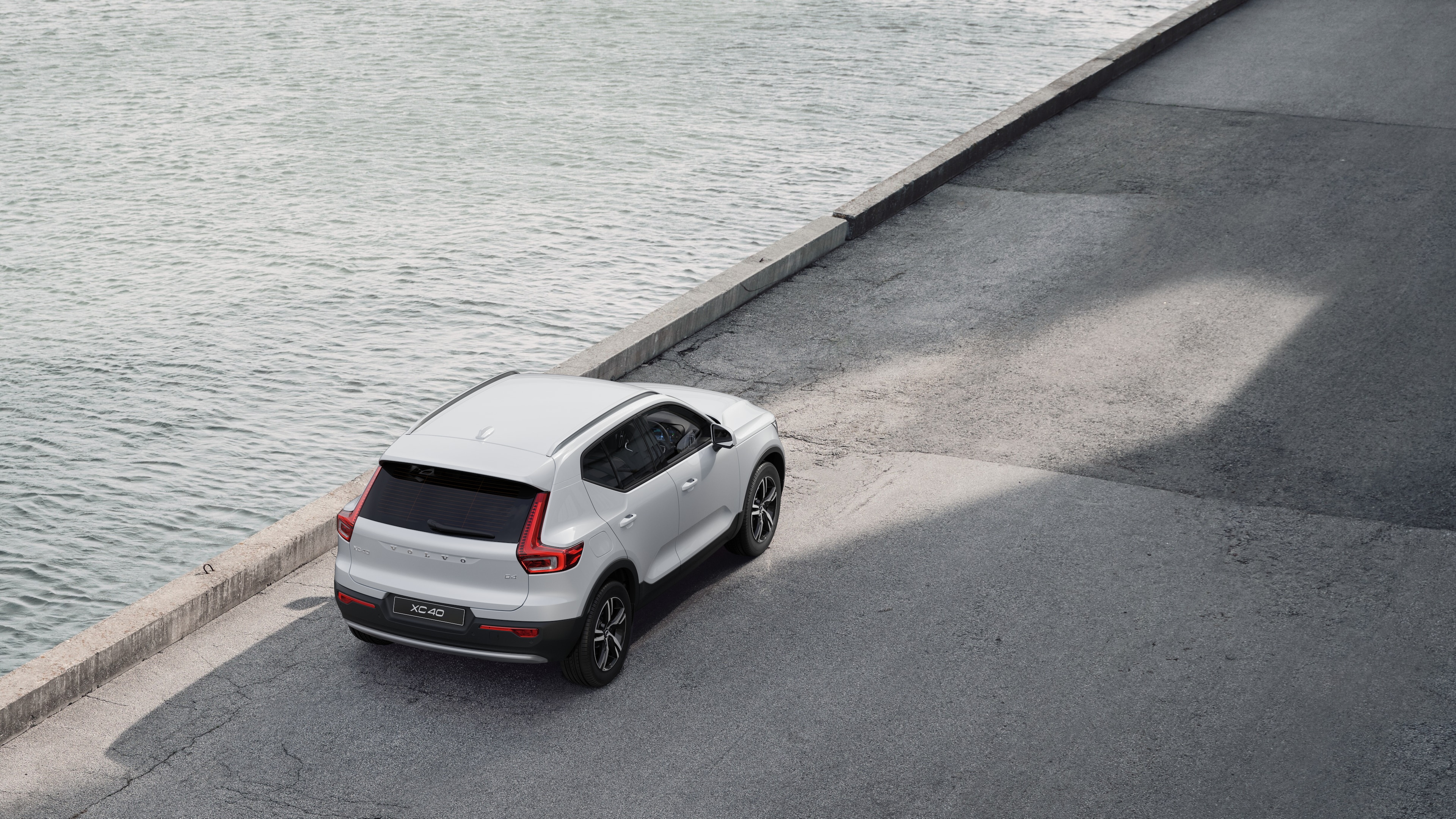 Volvo car rear view parked on quiet street beside water, with a paved walkway and water as the background.