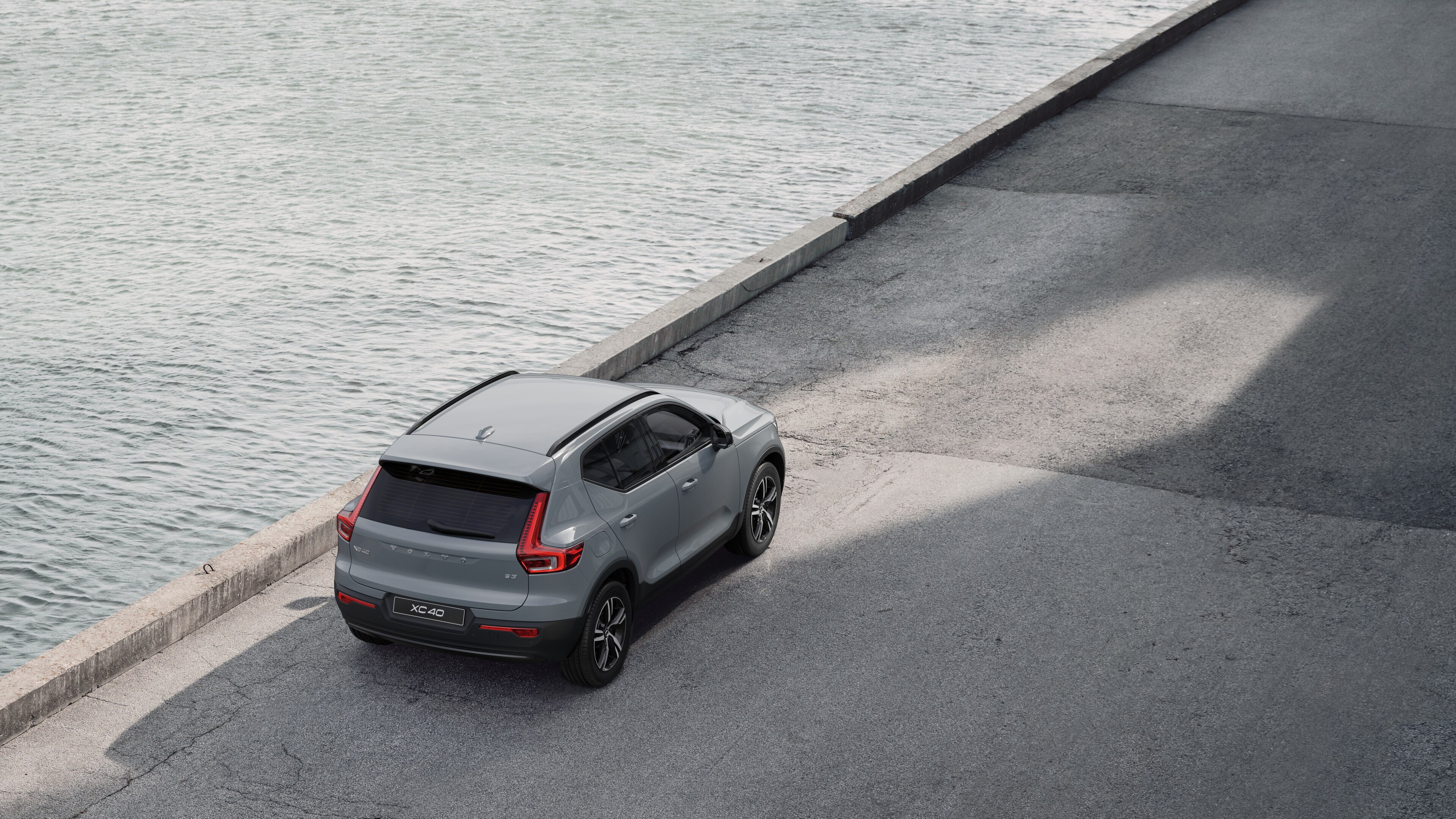 Achteraanzicht van een Volvo geparkeerd in een rustige straat aan het water, met een geplaveid looppad en water als achtergrond.