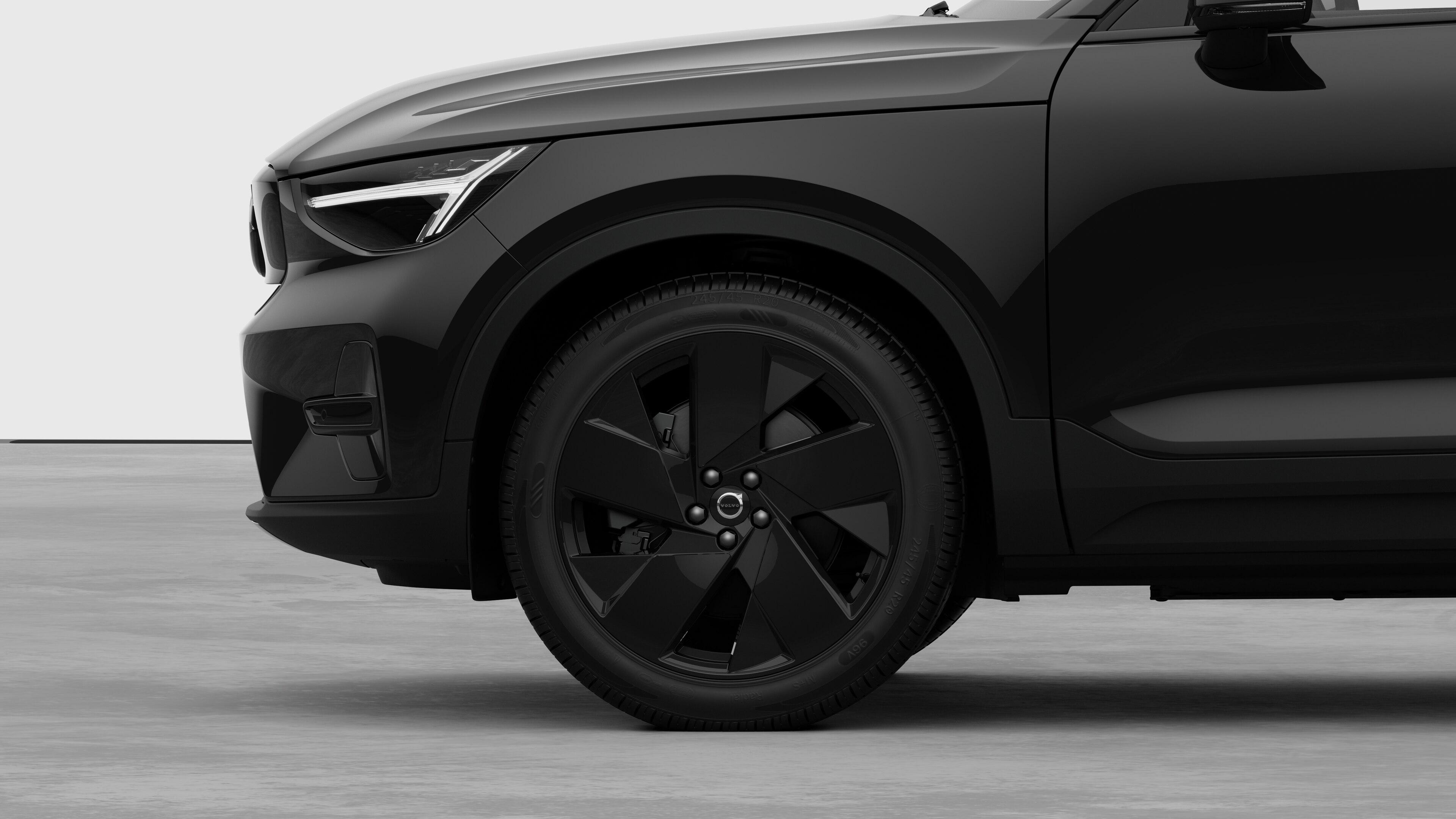 A Volvo autó külső oldalnézete, amely az első kerékre és a sárvédőre összpontosít, egyszerű stúdióháttér előtt.