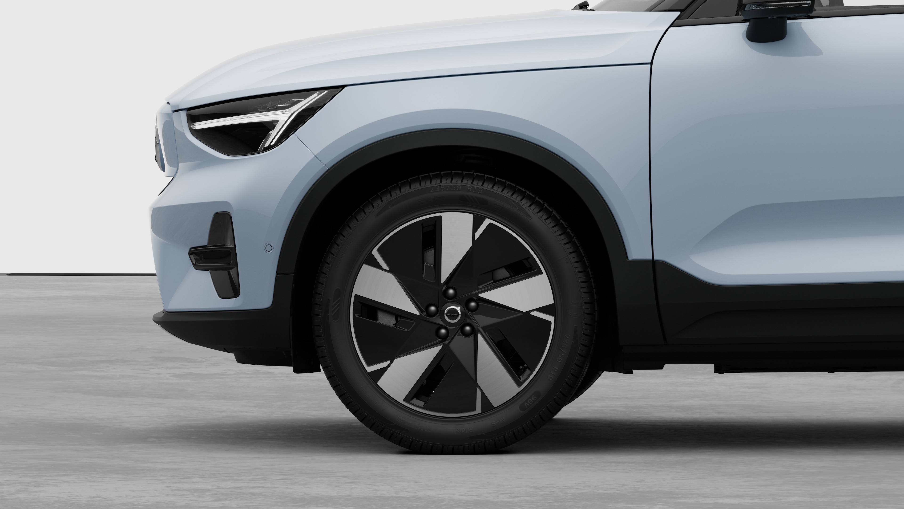 Düz bir stüdyo arka planına yerleştirilmiş, ön tekerleğe ve çamurluğa odaklanan Volvo otomobilin dış yandan görünümü.