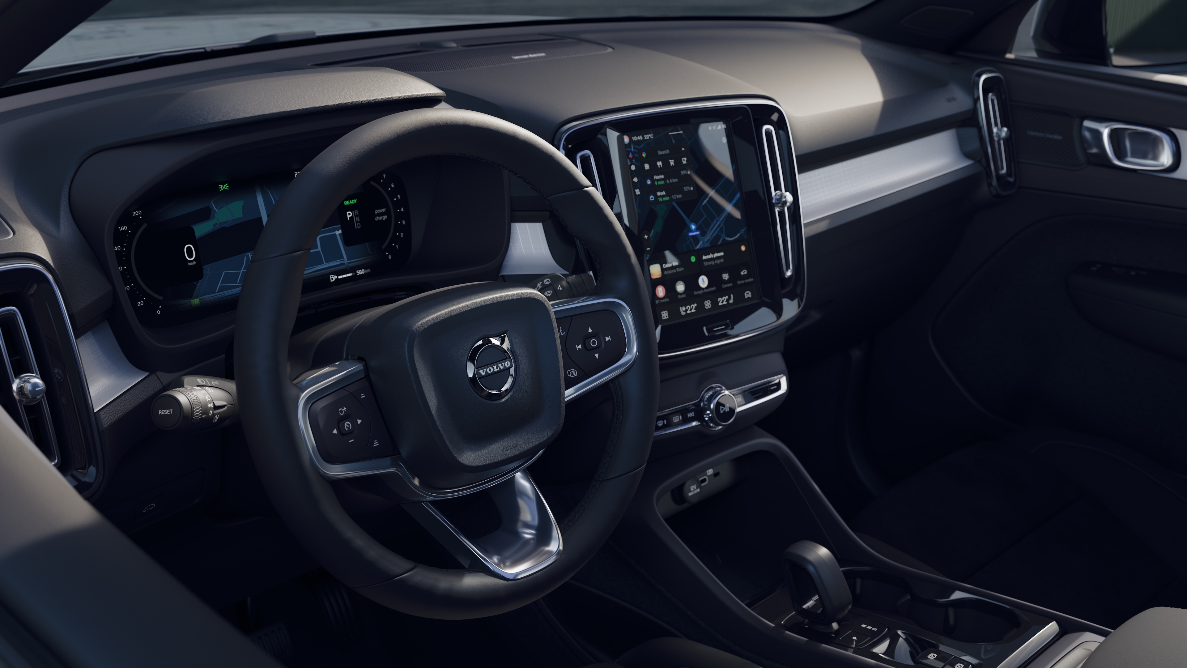 Interno di un'auto Volvo che mostra cruscotto, volante e console centrale con display digitale sullo sfondo di una strada aperta.