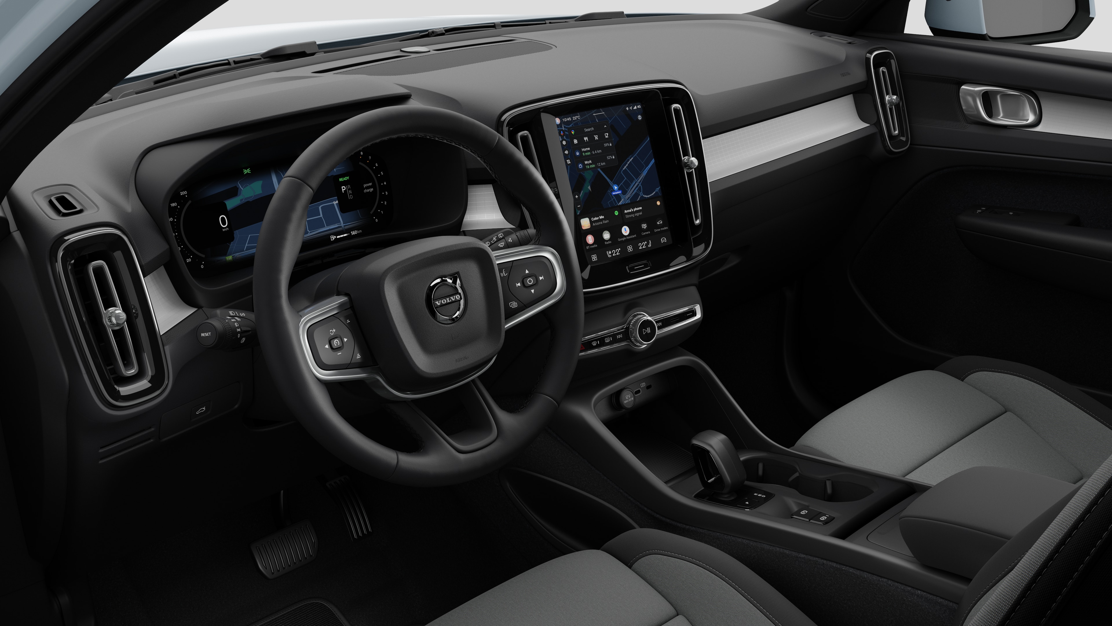 Interior view of a Volvo car showing the dashboard, steering wheel, center console, and digital display screen in a plain studio background.