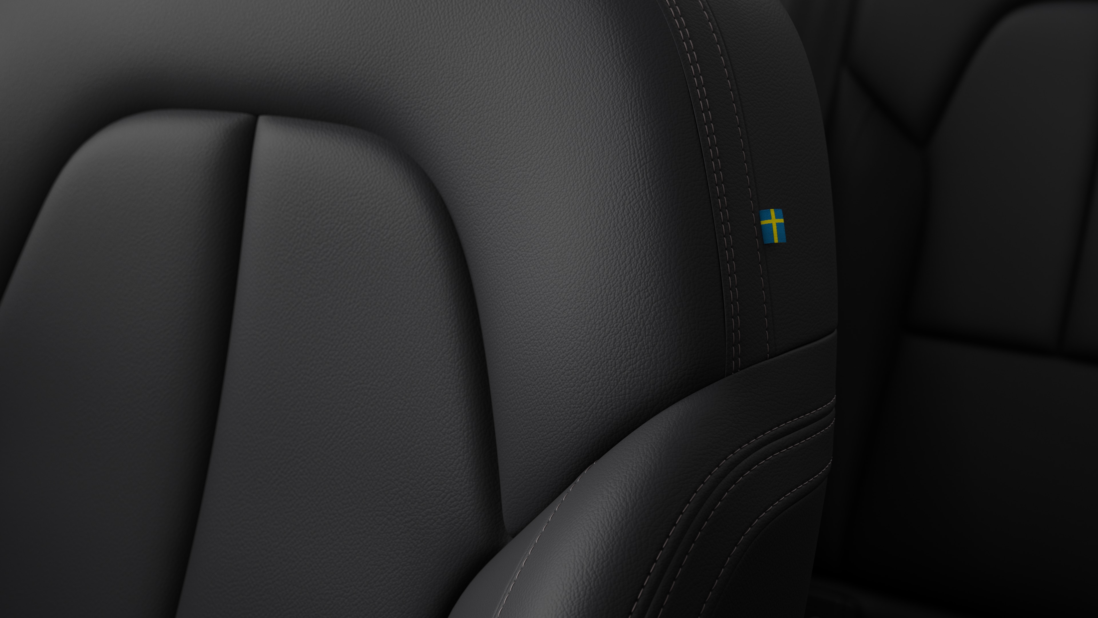 מבט מקרוב על פרטי עיצוב בפנים המושב של מכונית וולוו המציגים תפרים ותג דגל שוודיה קטן.