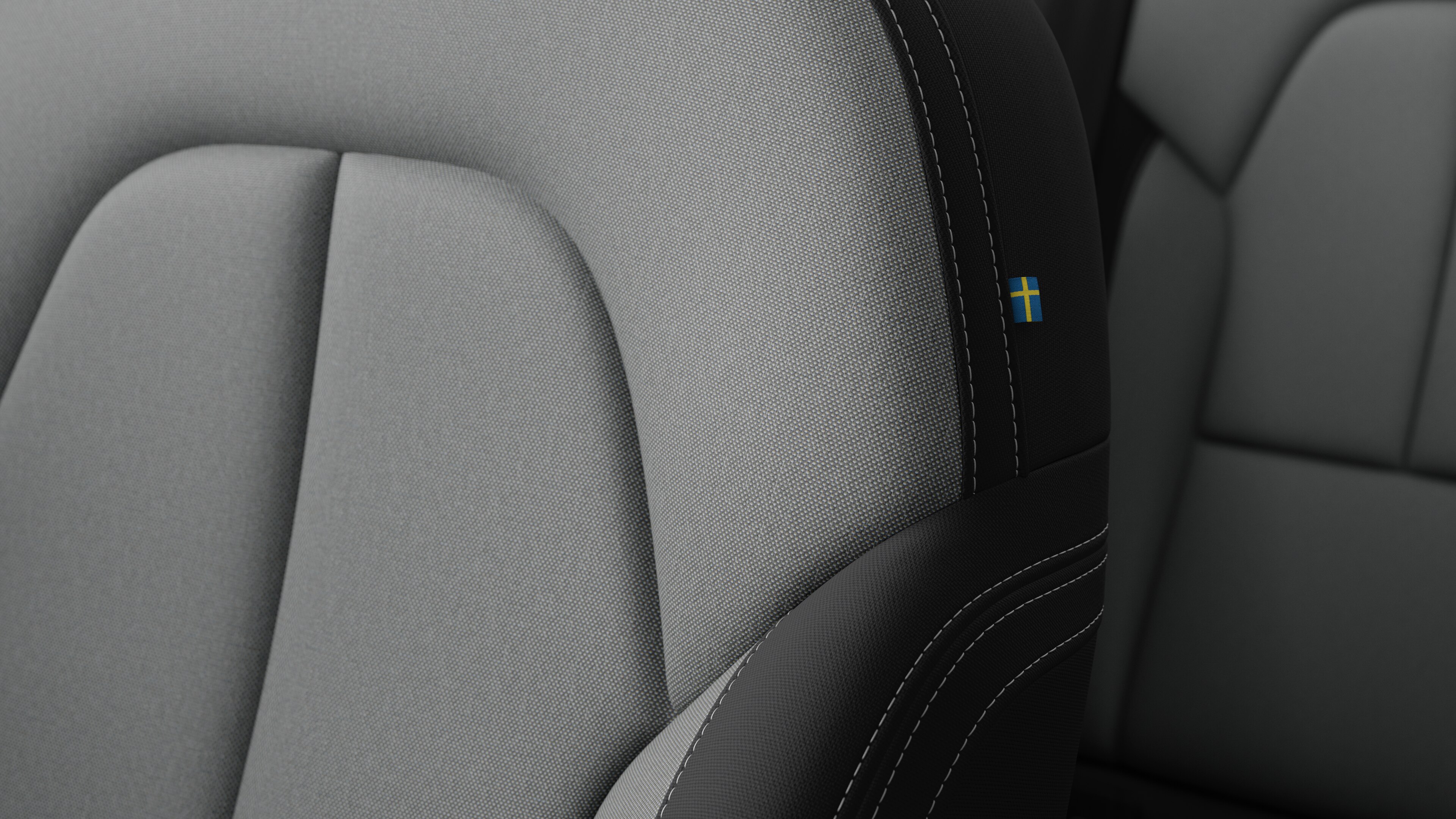 ვოლვოს მანქანის ინტერიერის სავარძლის დეტალების დახურვა, რომელიც აჩვენებს ნაკერს და პატარა შვედეთის დროშის ტეგს.