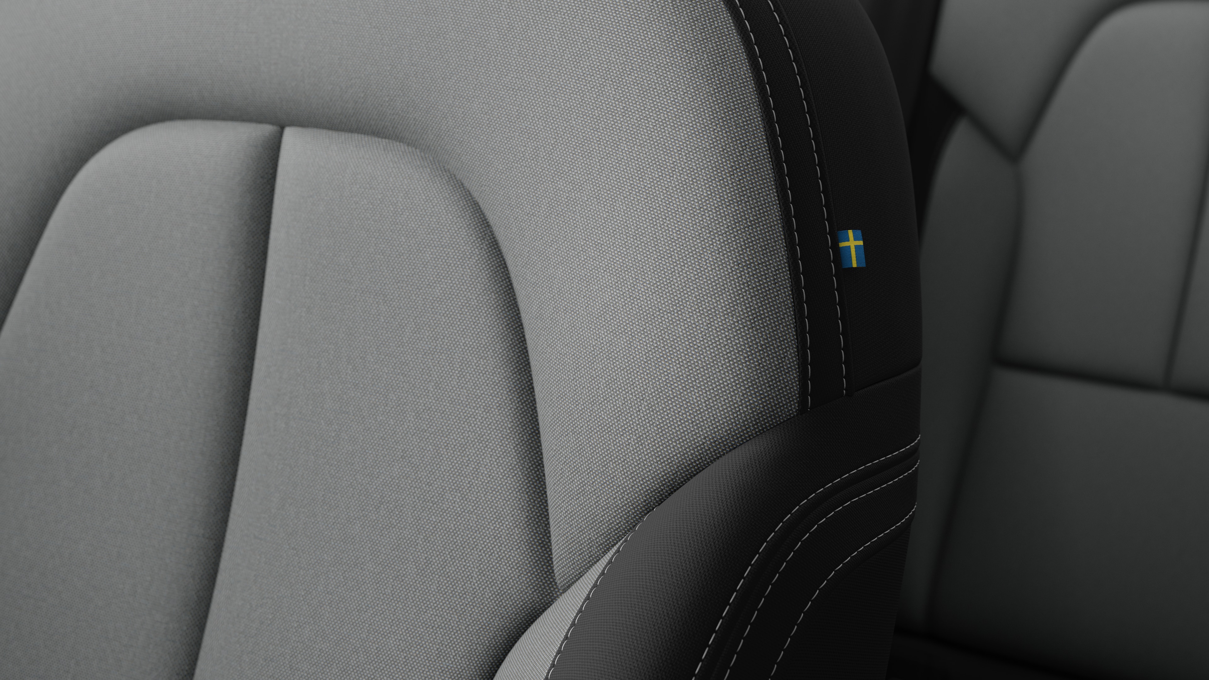 Närbild av Volvo Cars interiör, sätesdetalj som visar sömmar och en liten svensk flagga.