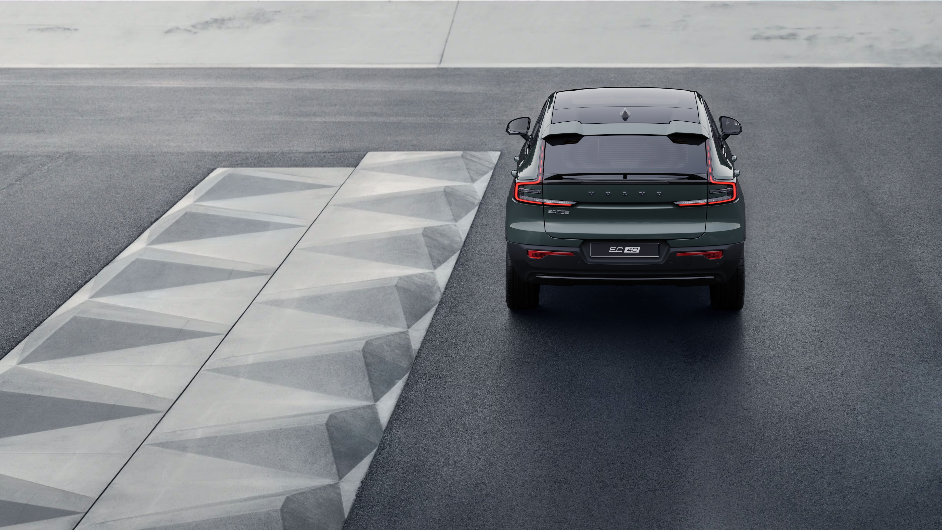 Volvo automašīnas aizmugures skats uz līkumotu piekrastes ceļu ar pludmales fonu.