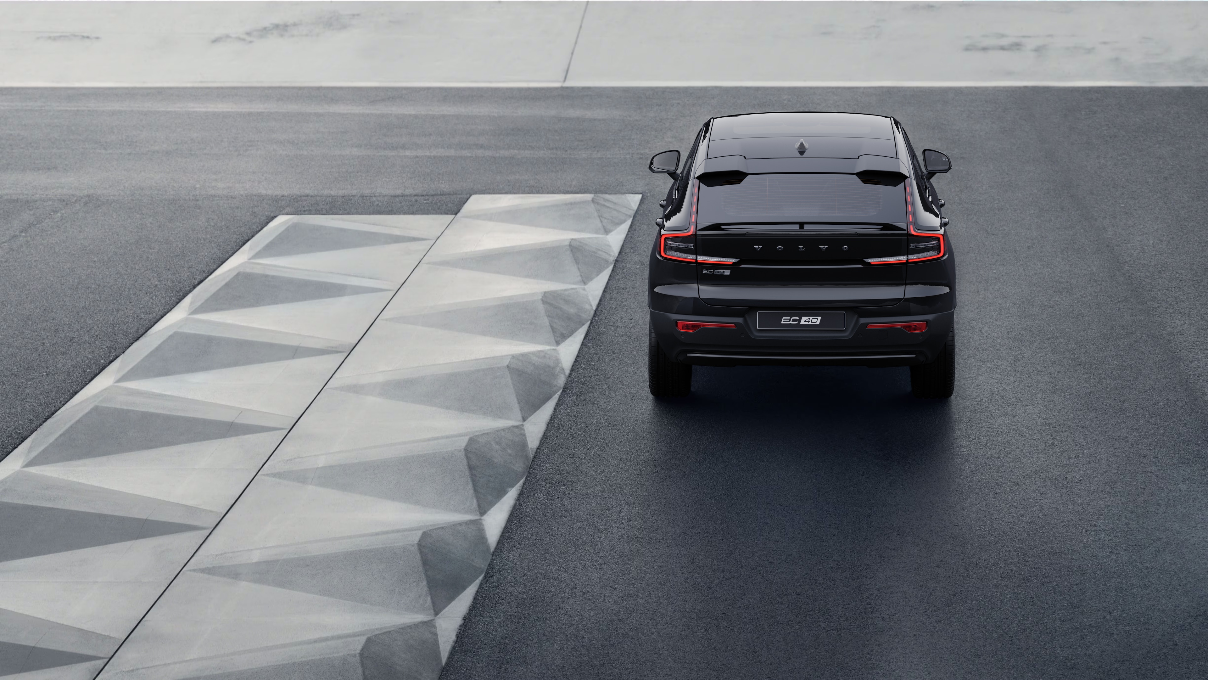 Volvo automašīnas aizmugures skats uz līkumotu piekrastes ceļu ar pludmales fonu.
