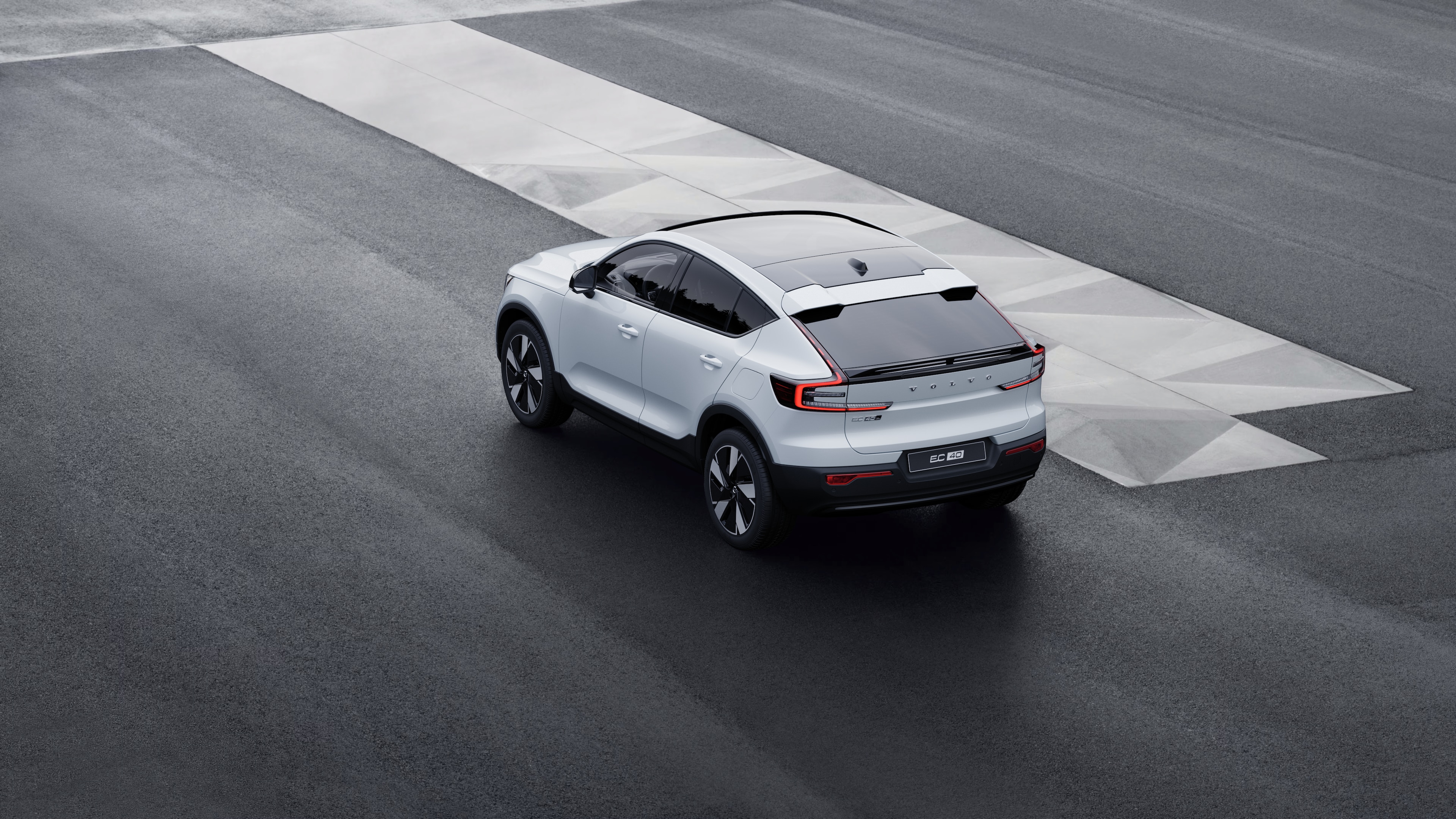 Volvo car in rear three-quarter view parked against a concrete wall on an urban street background.