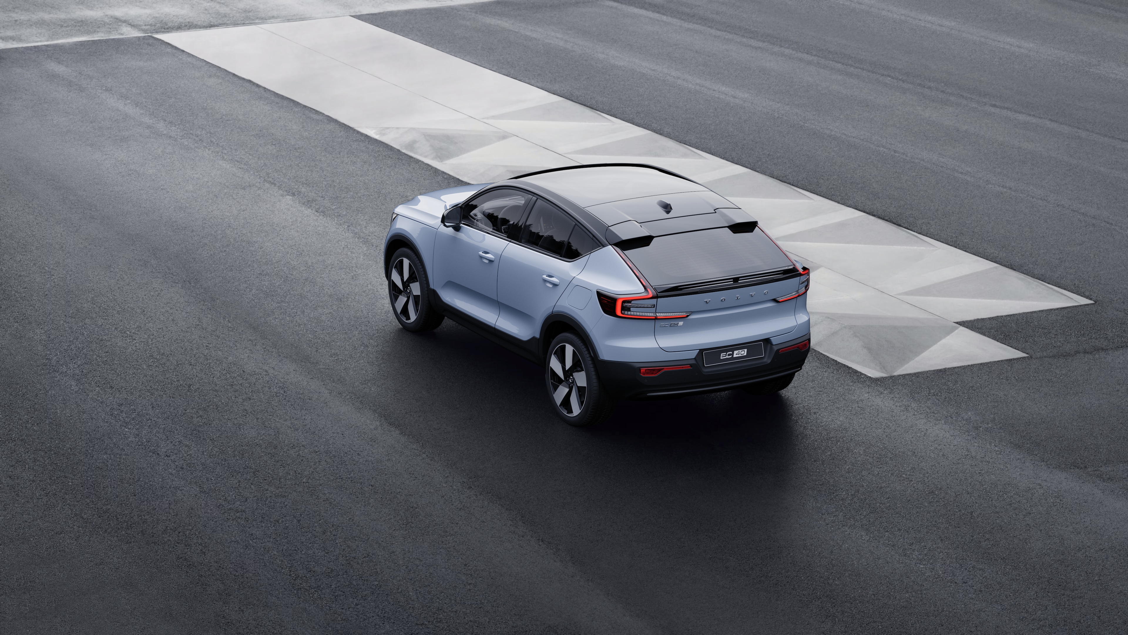 Vehículo Volvo en vista trasera de tres cuartos estacionado contra un muro de hormigón en un fondo de calle urbana.