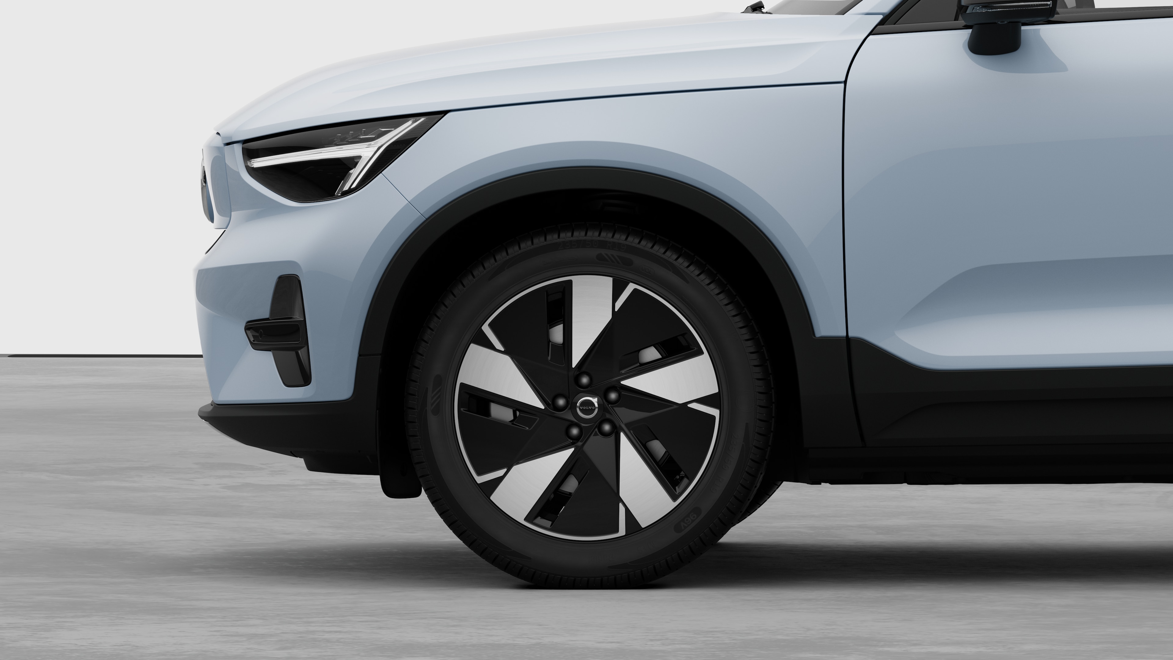 Volvo მანქანის გარე გვერდითი ხედი, რომელიც ფოკუსირებულია წინა ბორბალზე და ფენდერზე, დაყენებულია უბრალო სტუდიის ფონზე.