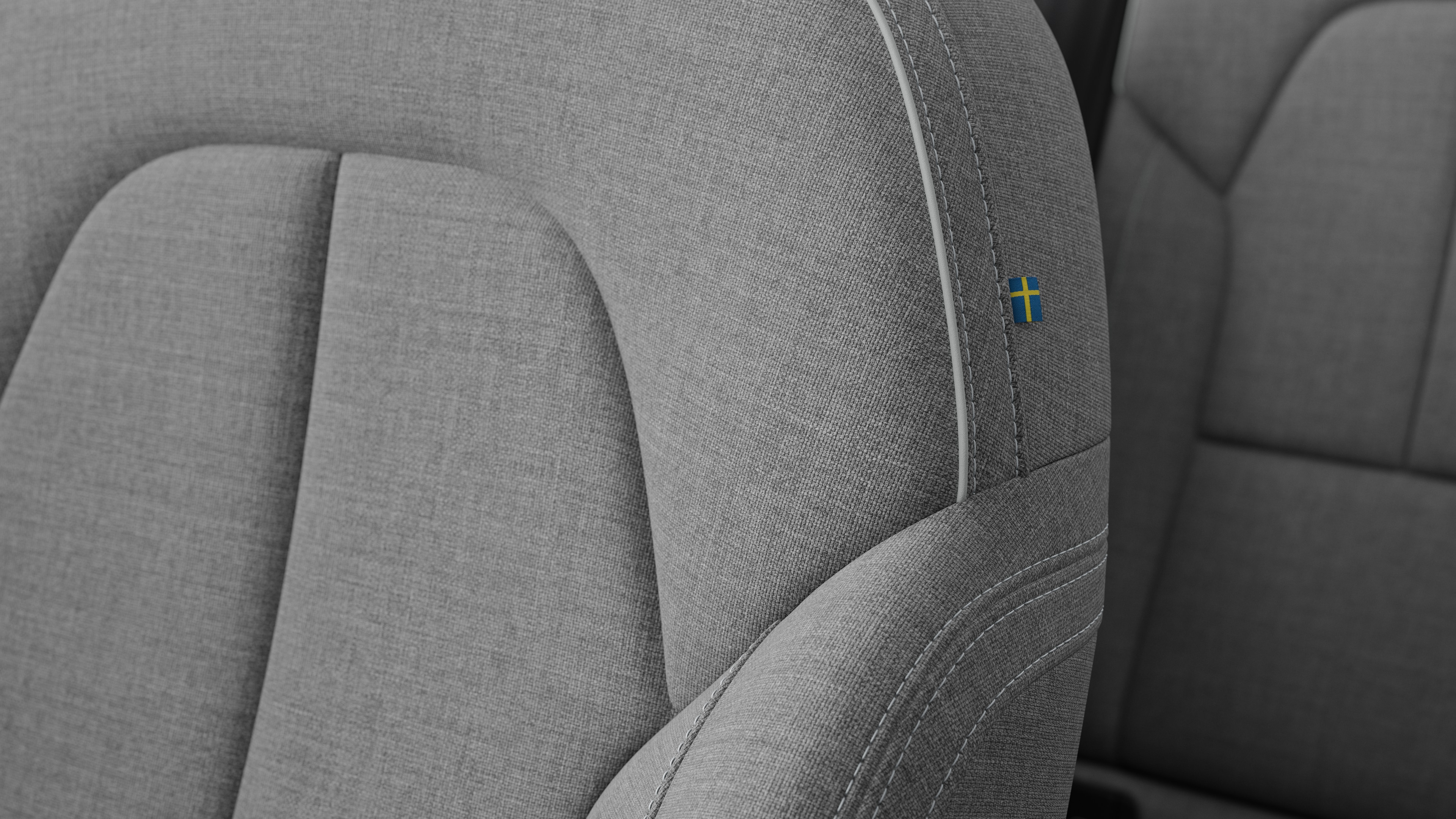 Close-up do detalhe do banco do interior do carro Volvo mostrando costuras e uma pequena etiqueta de bandeira sueca.