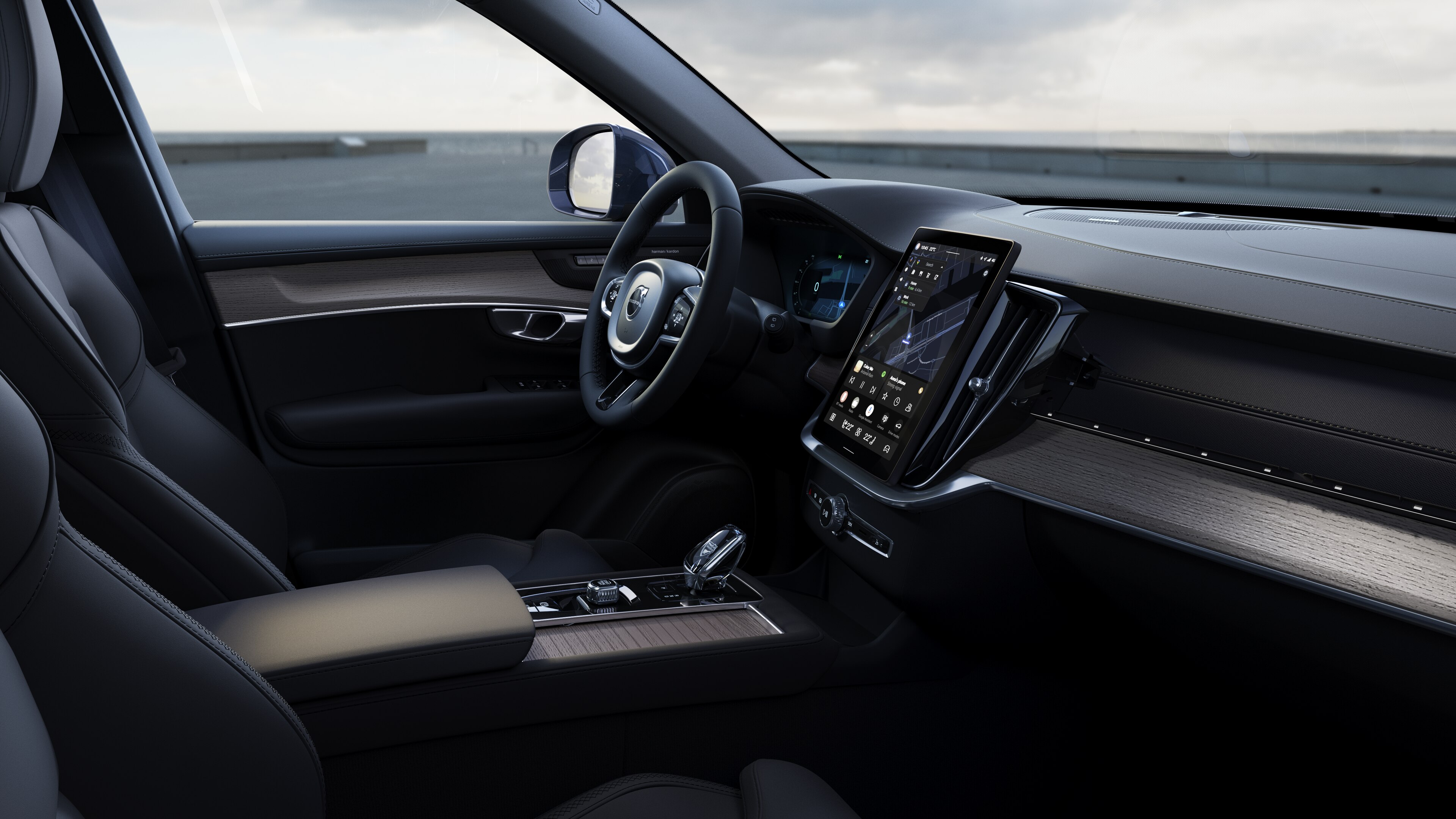 Interno di un'auto Volvo che mostra cruscotto, volante e console centrale con display digitale sullo sfondo di una strada aperta.