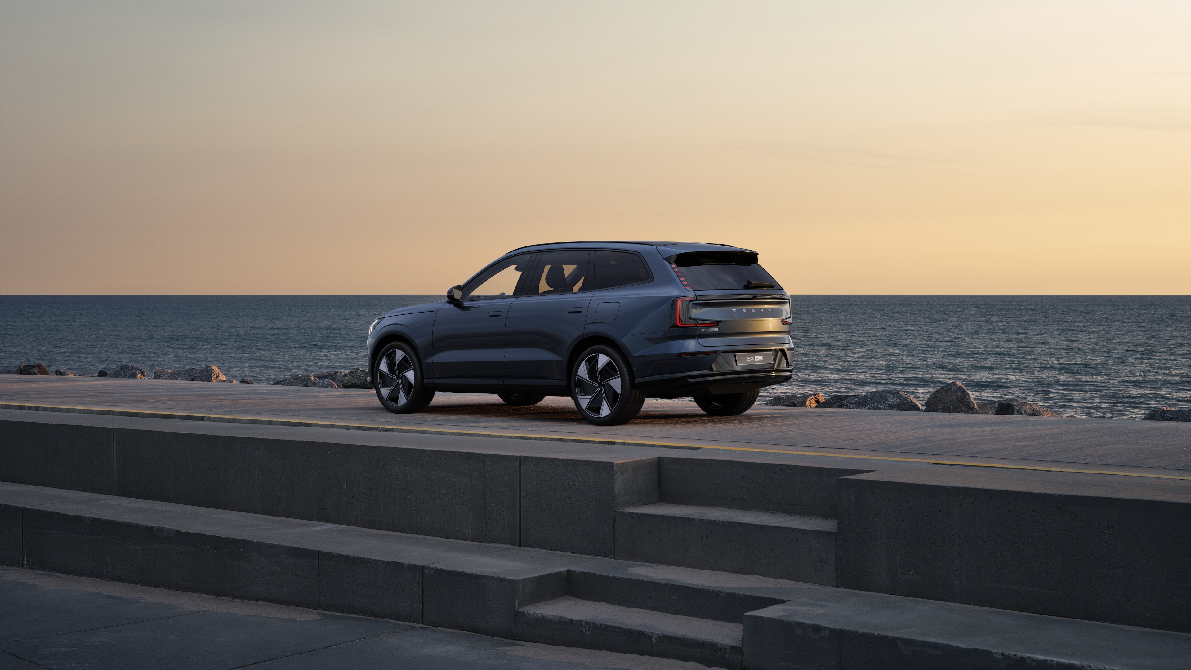 Volvo car in rear three-quarter view parked against a concrete wall on an urban street background.
